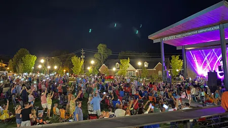 Crowd enjoying outdoor nighttime concert at Hardy Family Automotive Amphitheater with colorful stage lights.