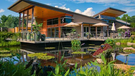 Modern building with large deck, outdoor tables, umbrellas, and pond with water lilies and greenery