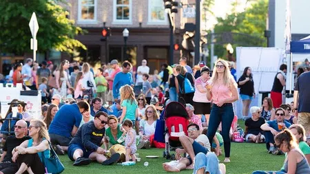 Crowd of people relaxing and socializing on grass at outdoor community event in sunny urban setting