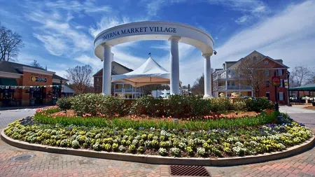 Smyrna Market Village entrance with white columns, colorful flower beds, and blue sky on a sunny day