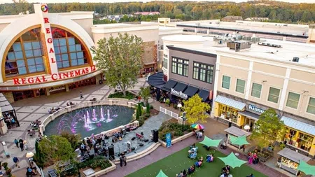 Aerial view of Regal Cinemas, outdoor fountain, shops, and people gathering in a lively plaza at sunset.