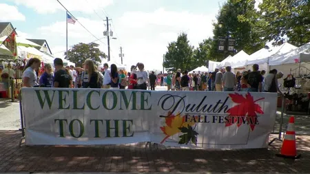 Crowd of people at Duluth Fall Festival with tents and a welcome banner on a sunny day.