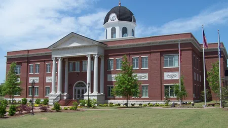 Red brick courthouse with white columns, clock tower, and American flags on a sunny day.