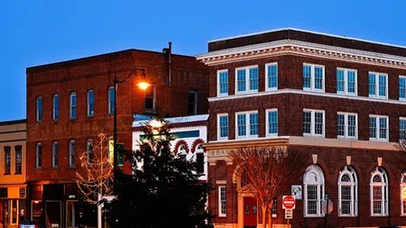 Historic brick buildings along a calm street at dusk with glowing street lamps and clear blue sky.