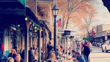 Outdoor street cafe with people dining under colorful lights on a sunny autumn day with fall trees.