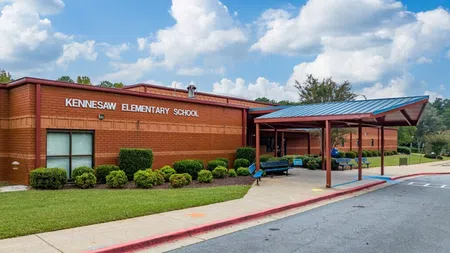 Kennesaw Elementary School brick building with covered entrance, benches, and landscaping under a partly cloudy sky