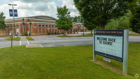 Exterior view of Sandy Springs Charter Middle School with welcome sign and surrounding greenery under cloudy sky