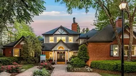 Elegant two-story house with brick and siding exterior surrounded by lush trees and garden at dusk