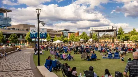 Crowd of people enjoying an outdoor concert at City Springs under a partly cloudy blue sky.