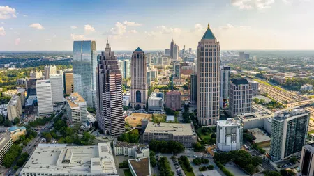 Aerial view of downtown Atlanta skyline with modern skyscrapers and highways under a partly cloudy sky.