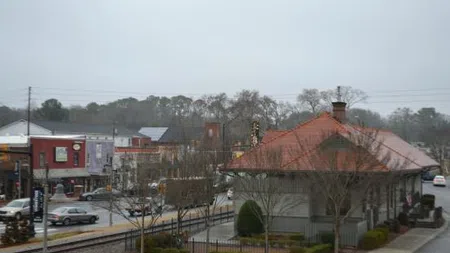 Historic train station near railway tracks in small town on an overcast day with surrounding buildings and cars.