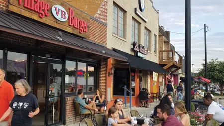 Outdoor dining scene at Village Burger with people seated and socializing on a sidewalk patio under clear sky.
