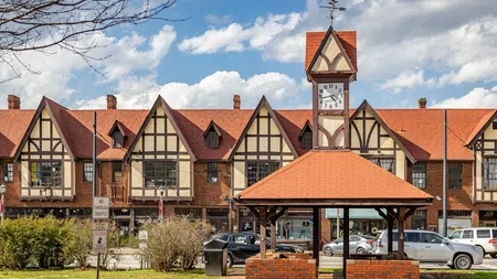Clock tower pavilion in front of Tudor-style buildings under a partly cloudy blue sky in a small town