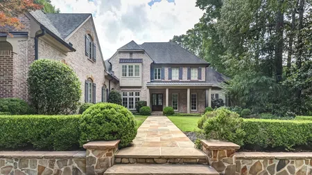 Elegant brick house with manicured landscaping, stone walkway, and lush green lawn under a partly cloudy sky