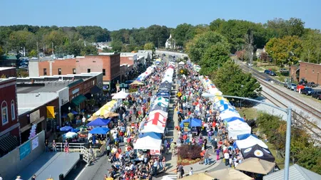 Aerial view of a bustling street market with colorful tents and crowds on a sunny day in a small town.