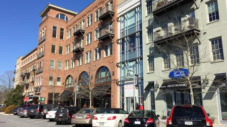 Street view of brick and modern buildings with parked cars and storefronts under clear blue sky