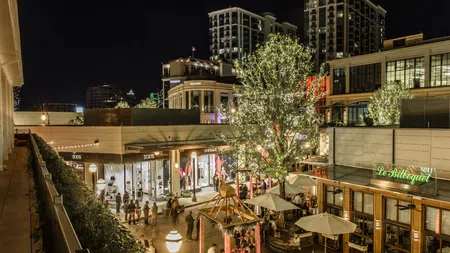 Nighttime urban shopping area with lit trees, outdoor dining, and modern buildings under a clear sky.