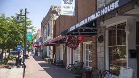 Sunlit sidewalk with shops including Stone Mountain Public House and downtown gallery signs on a quaint main street.