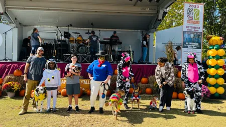 People and dogs in Halloween costumes pose in front of a stage decorated with pumpkins at autumn festival
