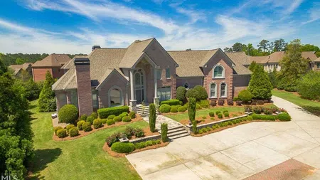 Large brick luxury home with manicured landscaping and a wide driveway under a blue sky