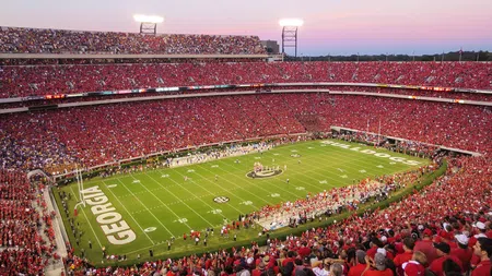 Crowded Georgia Bulldogs stadium at sunset during a college football game with fans dressed in red and yellow.