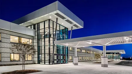 Modern school building with glass entrance and covered drop-off area at twilight under clear dark blue sky