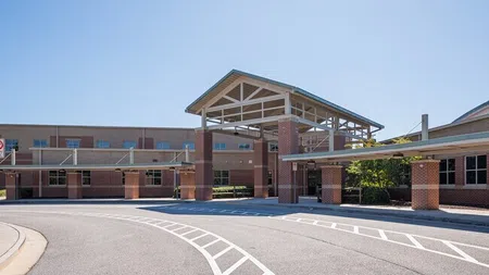 Modern school building entrance with covered drop-off area and clear blue sky on a sunny day.