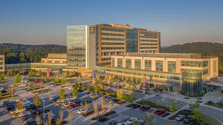 Modern hospital building with multiple floors and large parking lot during daytime with clear sky.