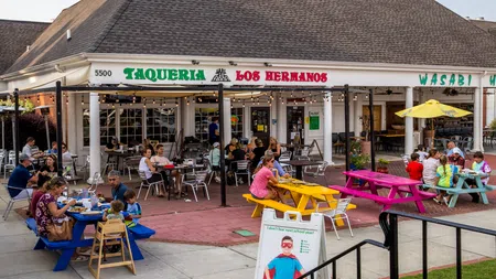 Outdoor dining scene at Taqueria Los Hermanos with colorful picnic tables and people enjoying meals.