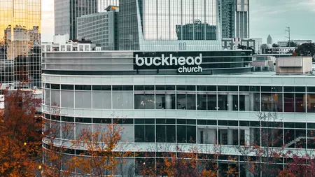 Modern glass building of Buckhead Church in downtown area with autumn trees and surrounding skyscrapers.