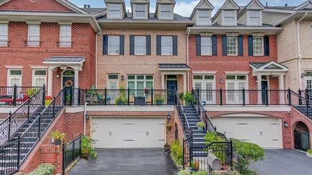 Row of modern brick townhouses with garages, front porches, stairs, and black railings under a partly cloudy sky
