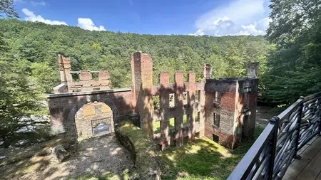 Ruins of an old brick building surrounded by green forest under a blue sky with clouds