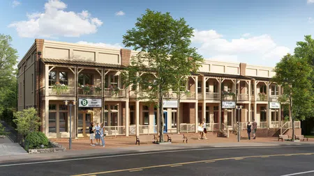 Two-story brick and beige commercial building with balconies, store signs, trees, and pedestrians on a sunny day.