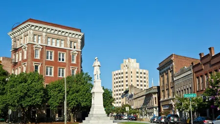 Historic downtown street with a white statue, classic brick buildings, and parked cars under a clear blue sky