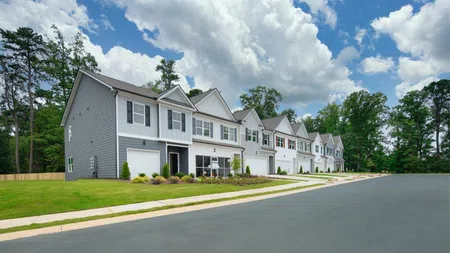 Row of modern townhouses with well-kept lawns under a partly cloudy sky in a suburban neighborhood.