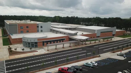 Aerial view of a large modern school building with a circular entrance and spacious parking lot under cloudy sky.