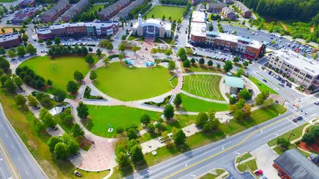 Aerial view of a town square with green park, amphitheater, surrounding shops, and busy roads