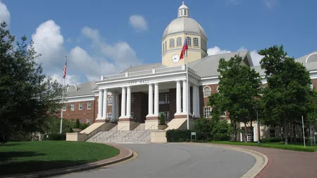 City Hall building with white columns, dome, flags, and curved driveway under a blue sky
