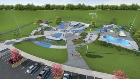 Aerial view of a modern skate park with circular ramps, a pool, greenery, and adjacent parking lot under clear sky