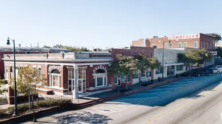 Historic brick buildings along a quiet street with trees and empty parking spaces in a small town.