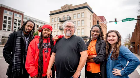 Group of five diverse adults smiling and posing together in an urban street setting with buildings behind them.
