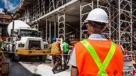 Construction workers in safety gear at an active building site with scaffolding and cement truck.
