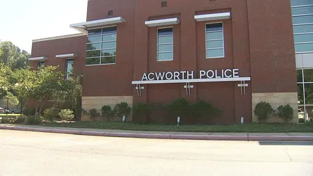 Brick building with Acworth Police sign on the exterior wall surrounded by greenery and clear sky.