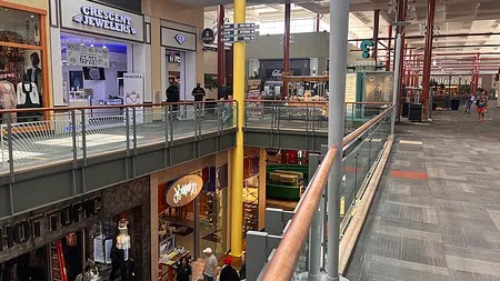 Indoor mall walkway with stores including Crescent Jewelers and Hot Topic, shoppers walking on both levels.