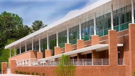 Modern brick building with large windows, white roof overhang, and outdoor patio seating surrounded by greenery.