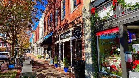 Sunny small-town street with brick buildings, colorful autumn trees, sidewalk cafes, and holiday decorations.