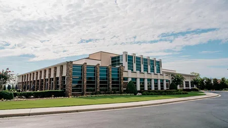 Modern office building with large windows, stone accents, and landscaped surroundings under a partly cloudy sky