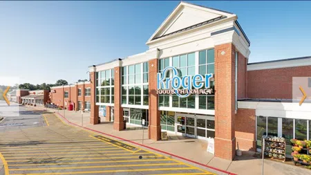Exterior view of a Kroger grocery store with large windows and clear signage under a sunny blue sky.