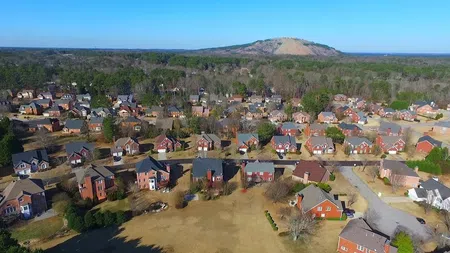 Aerial view of a suburban neighborhood with brick houses and a mountain in the background under a clear blue sky.