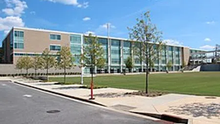 Modern glass and brick building with green lawn and young trees under a blue sky with clouds